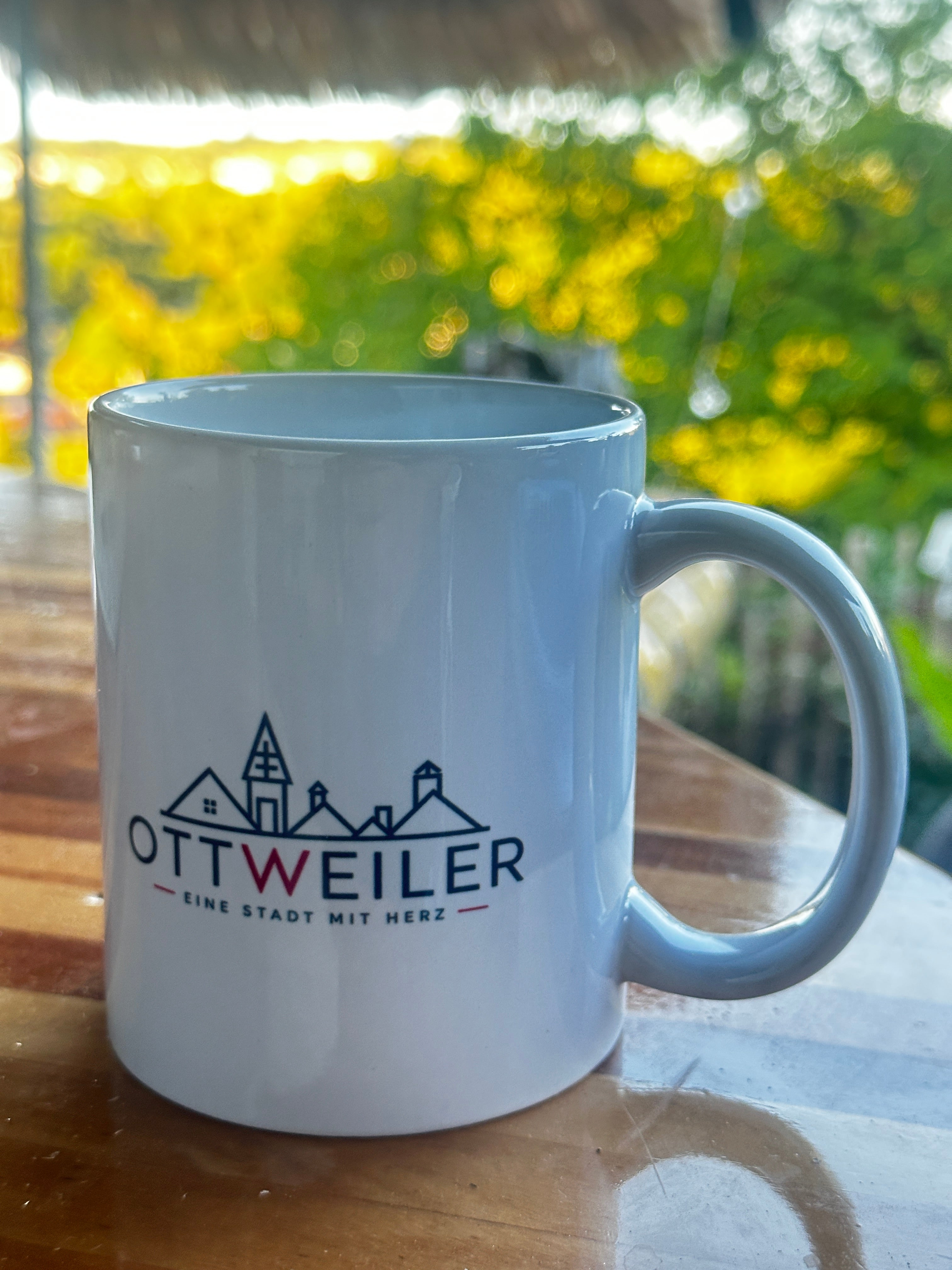Weiße Ottweiler Tasse mit Stadtsilhouette und Schriftzug „Eine Stadt mit Herz“ auf einem Holztisch